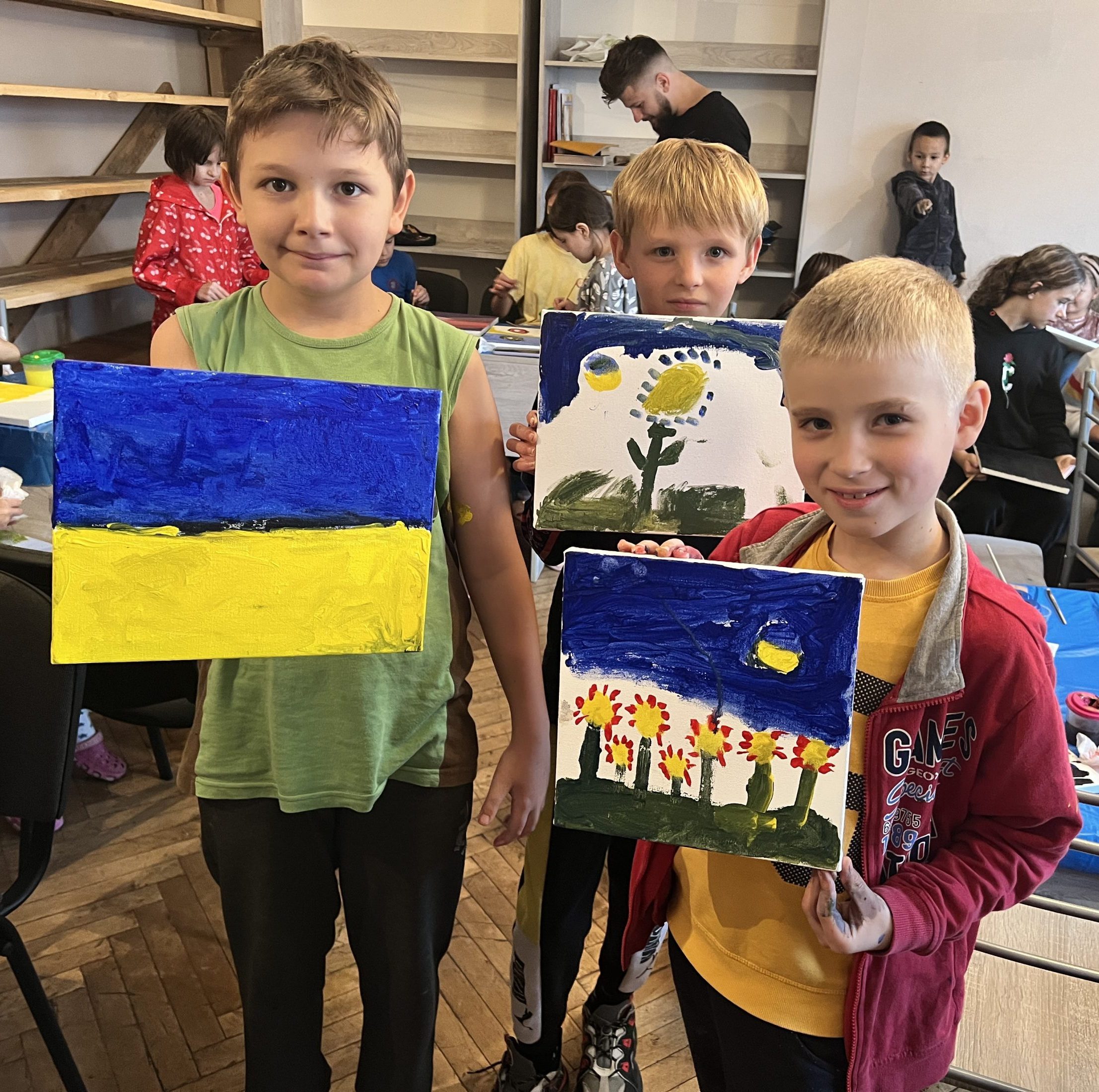Three children painting Ukrainian-inspired artwork at a shelter in Ukraine.